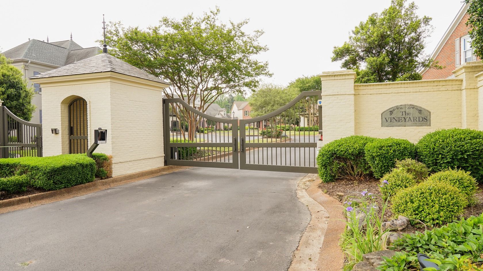 A large gate is surrounded by bushes and trees in a gated community.