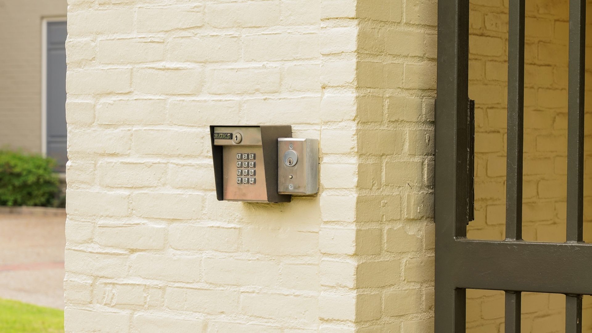 There is a key box on the side of a brick wall next to a gate.