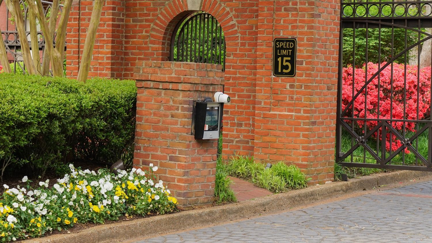 A brick wall with a gate and flowers in front of it.