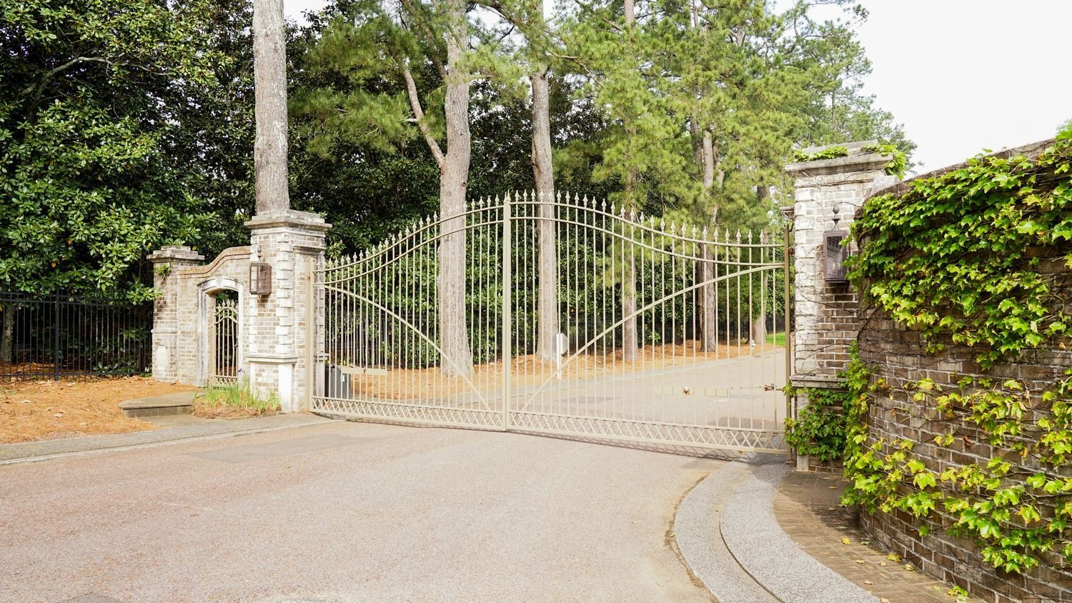 A metal gate is surrounded by trees and a stone wall.