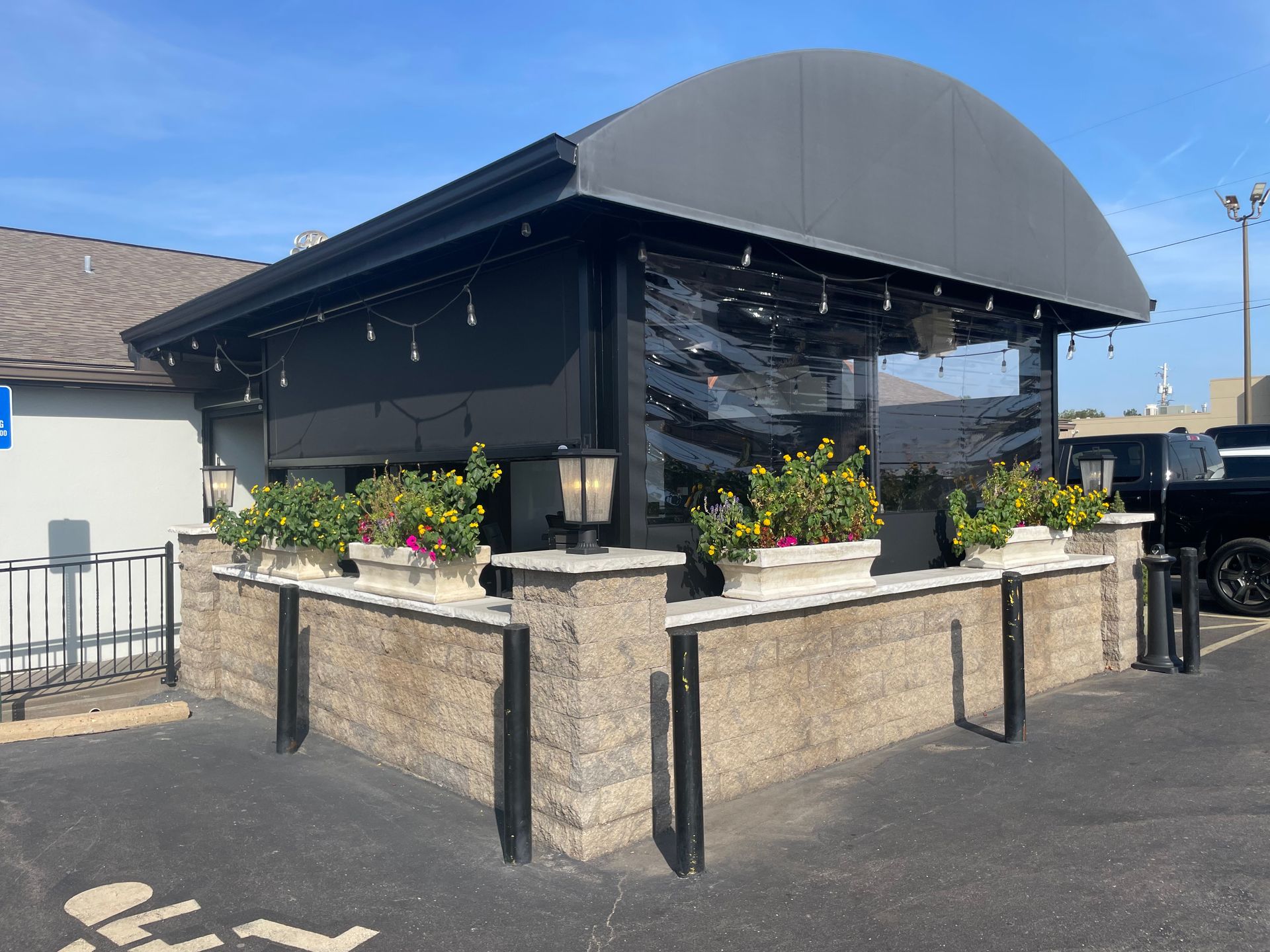 Outdoor restaurant seating with black awning, clear plastic sides, and flower boxes.