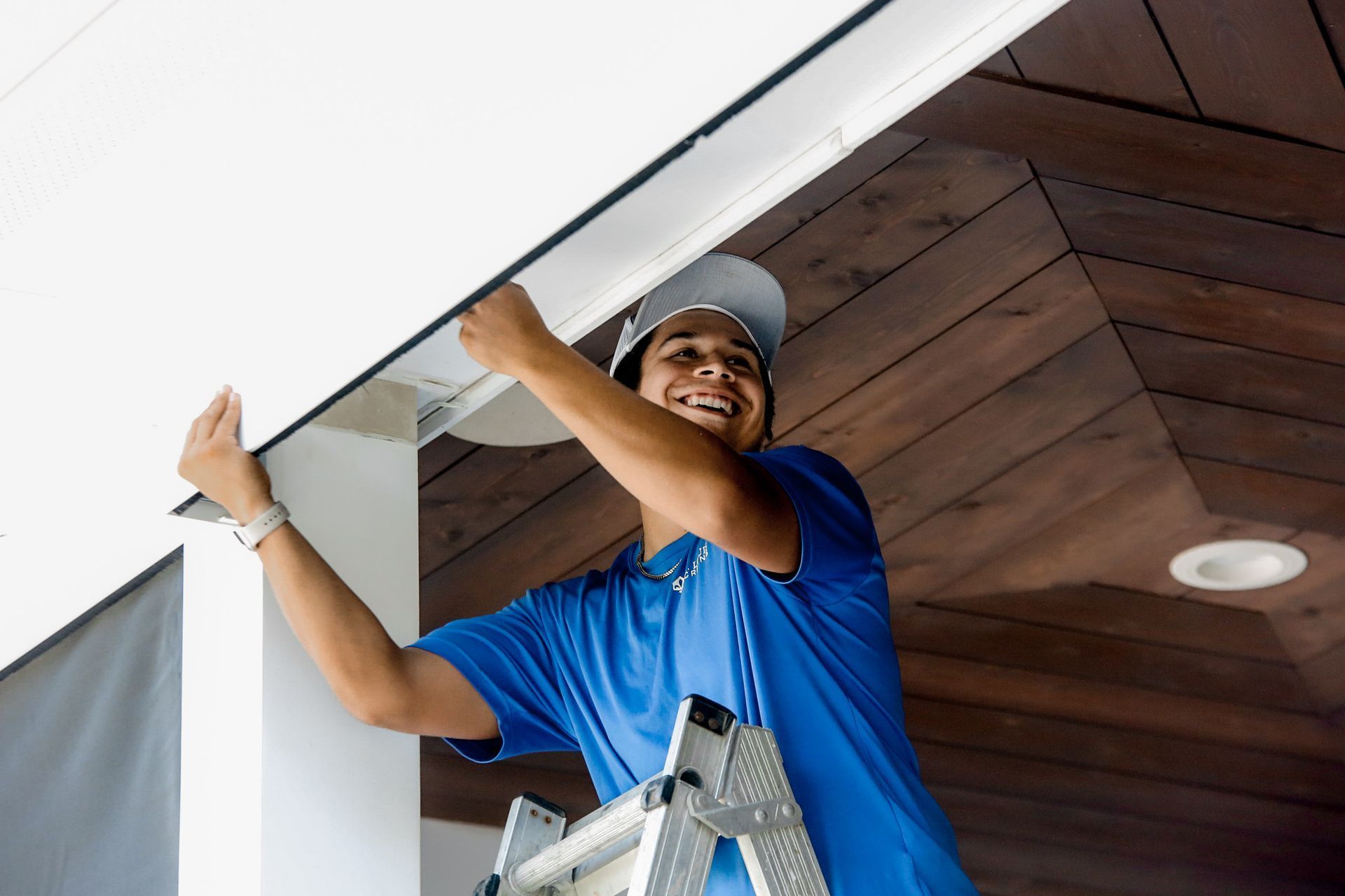 Worker in blue shirt installing ceiling panels on a ladder indoors