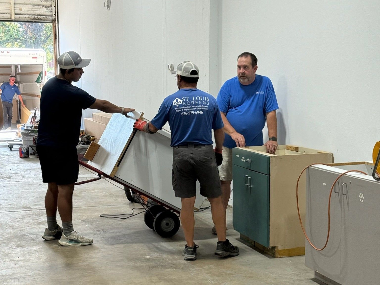 Three workers load boxes onto a hand truck in a warehouse or moving area.