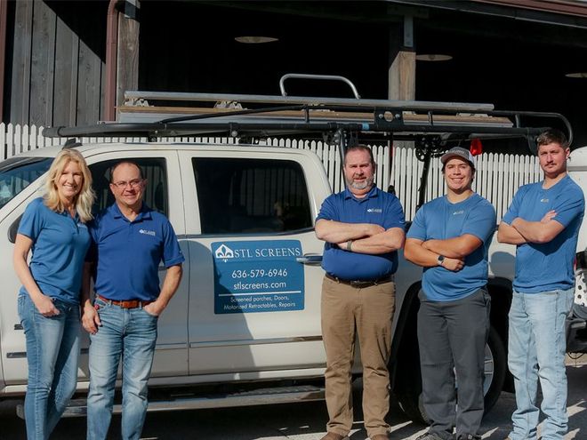 Five people stand next to a white truck with a rack. They wear blue shirts, one with arms crossed.