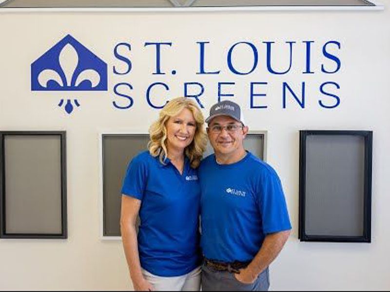 Two people in blue shirts posing in front of a St. Louis Screens logo.