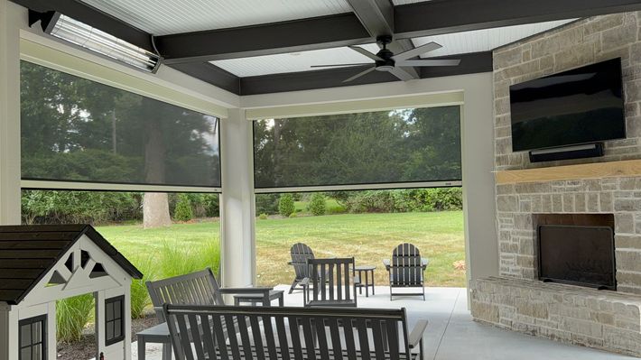 Covered patio with dining table, chairs, grill, and fireplace overlooking a green yard.