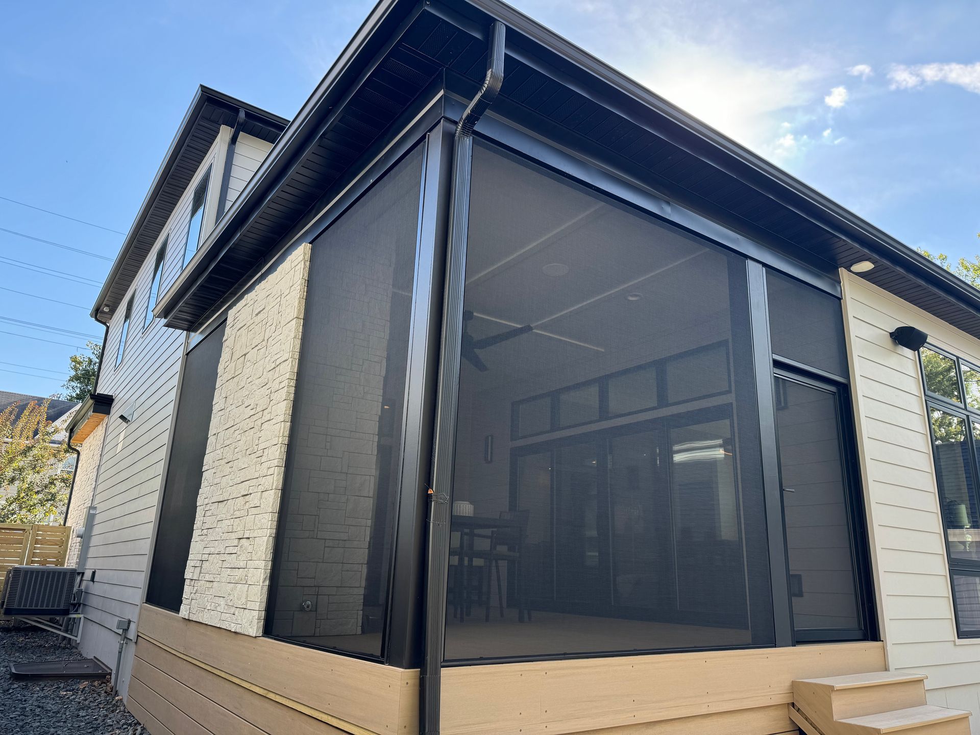 Screened-in porch attached to a house. Black screens and trim. Tan siding and decking.