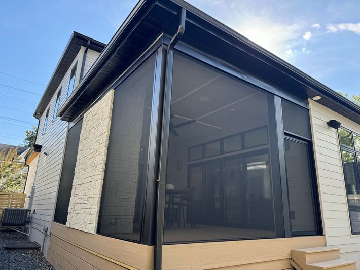 Corner view of a house with black mesh patio screens and white brick walls under a blue sky.