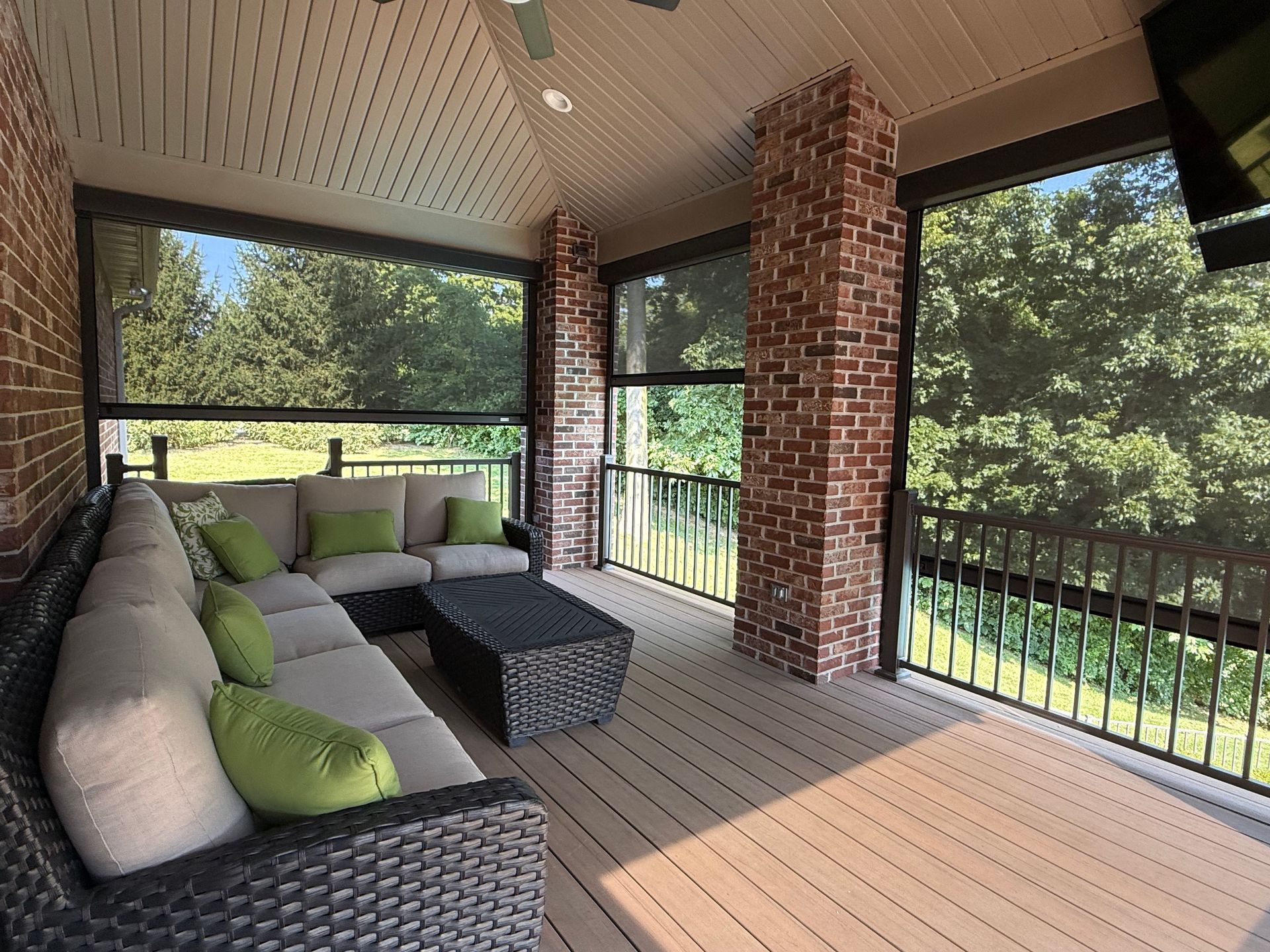 Covered outdoor patio with sectional sofa, green pillows, and roll-down screens.