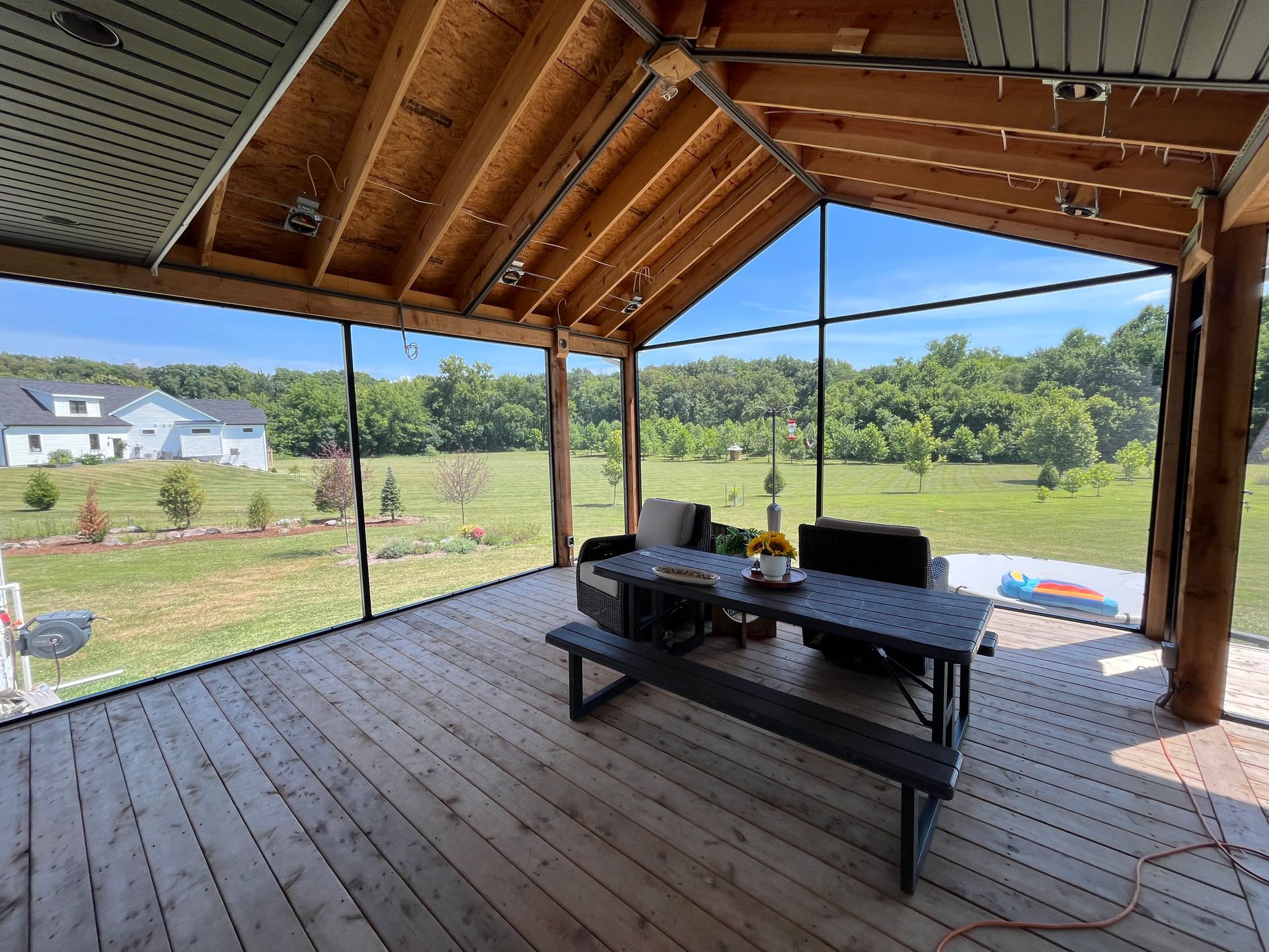 Screened-in porch with wooden deck and table. Backyard view with trees and blue sky.