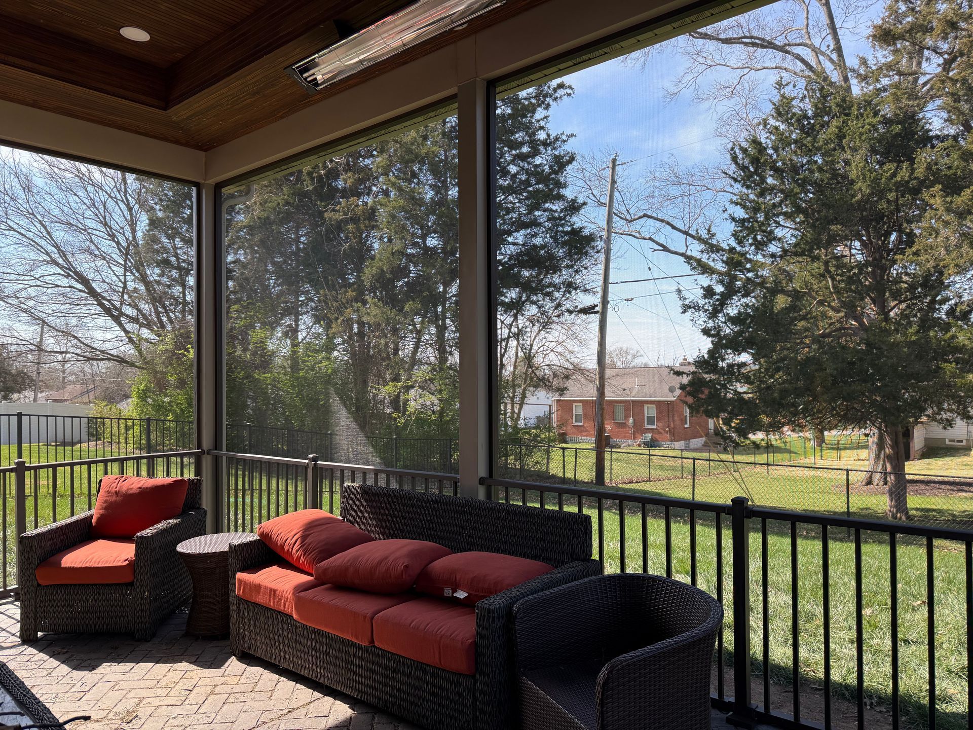 Screened porch with orange cushions, overlooking a yard with trees and a house.