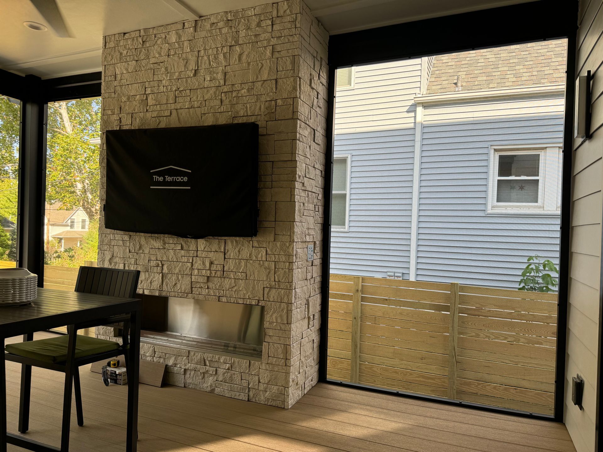 Living room corner: stone fireplace, TV, dining table, large window with a view of a house.