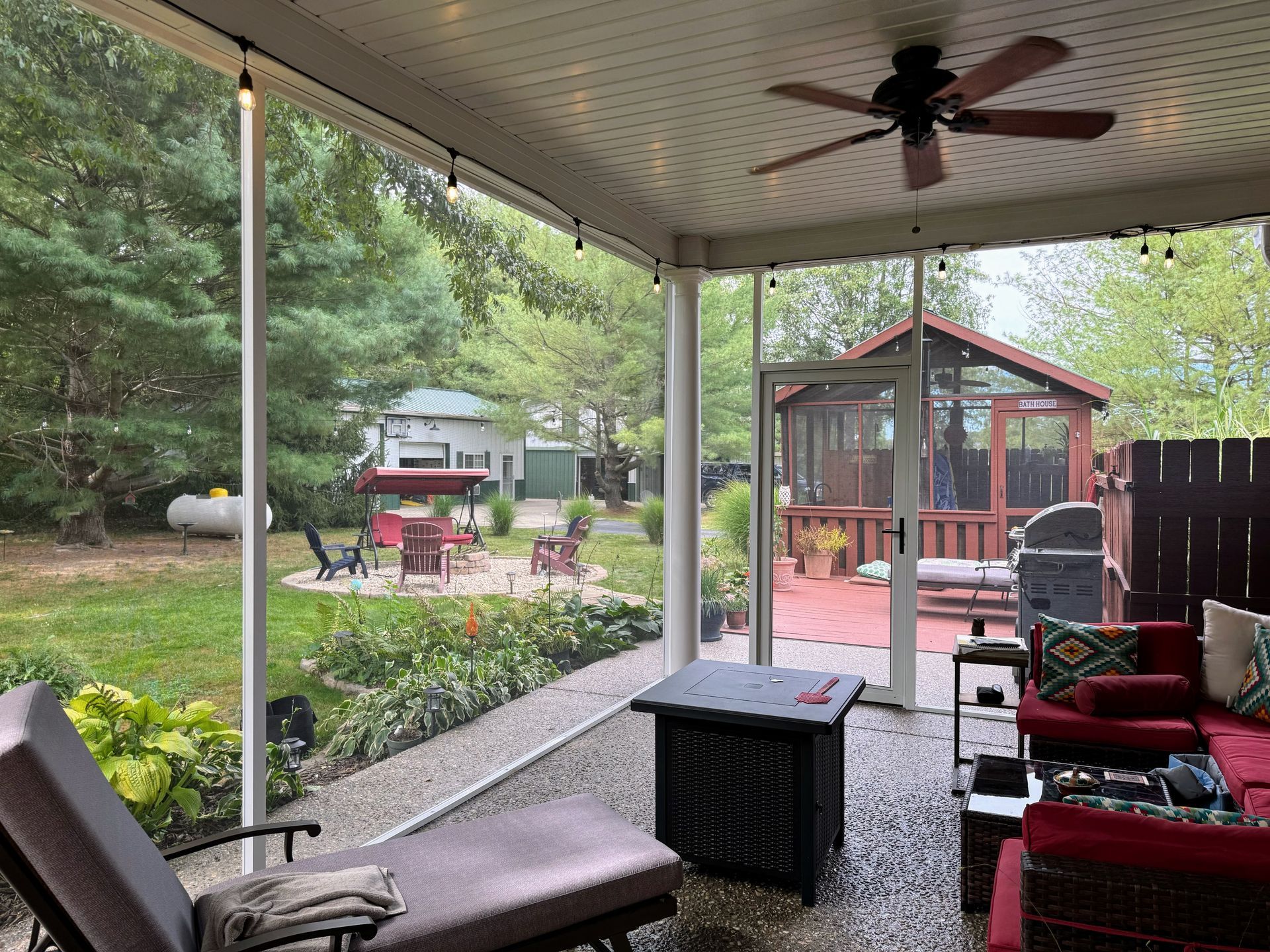 Screened porch with outdoor seating and view of a backyard with a fire pit, gazebo, and trees.