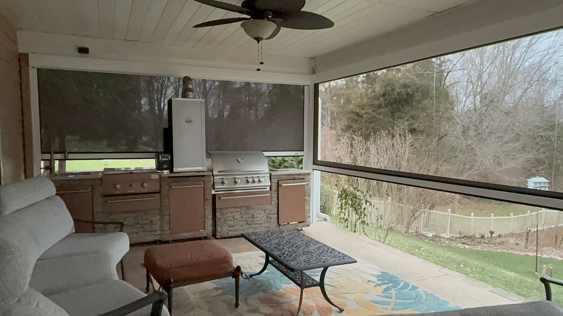 Covered outdoor kitchen with grill, cabinets, seating, and screen enclosure.