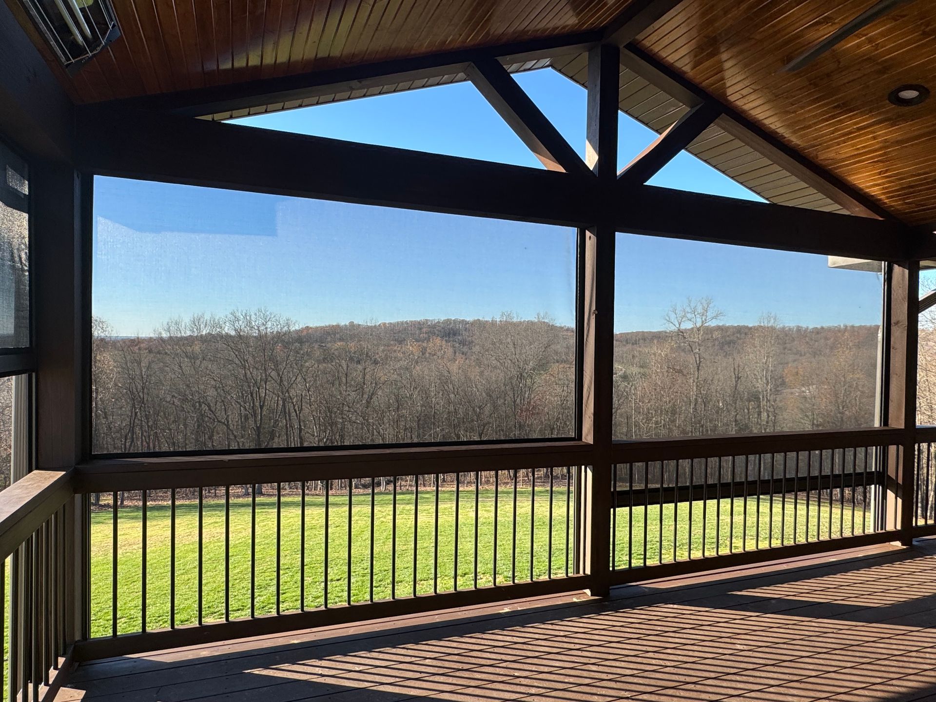 A screened porch with a view of a grassy field and trees under a clear blue sky.