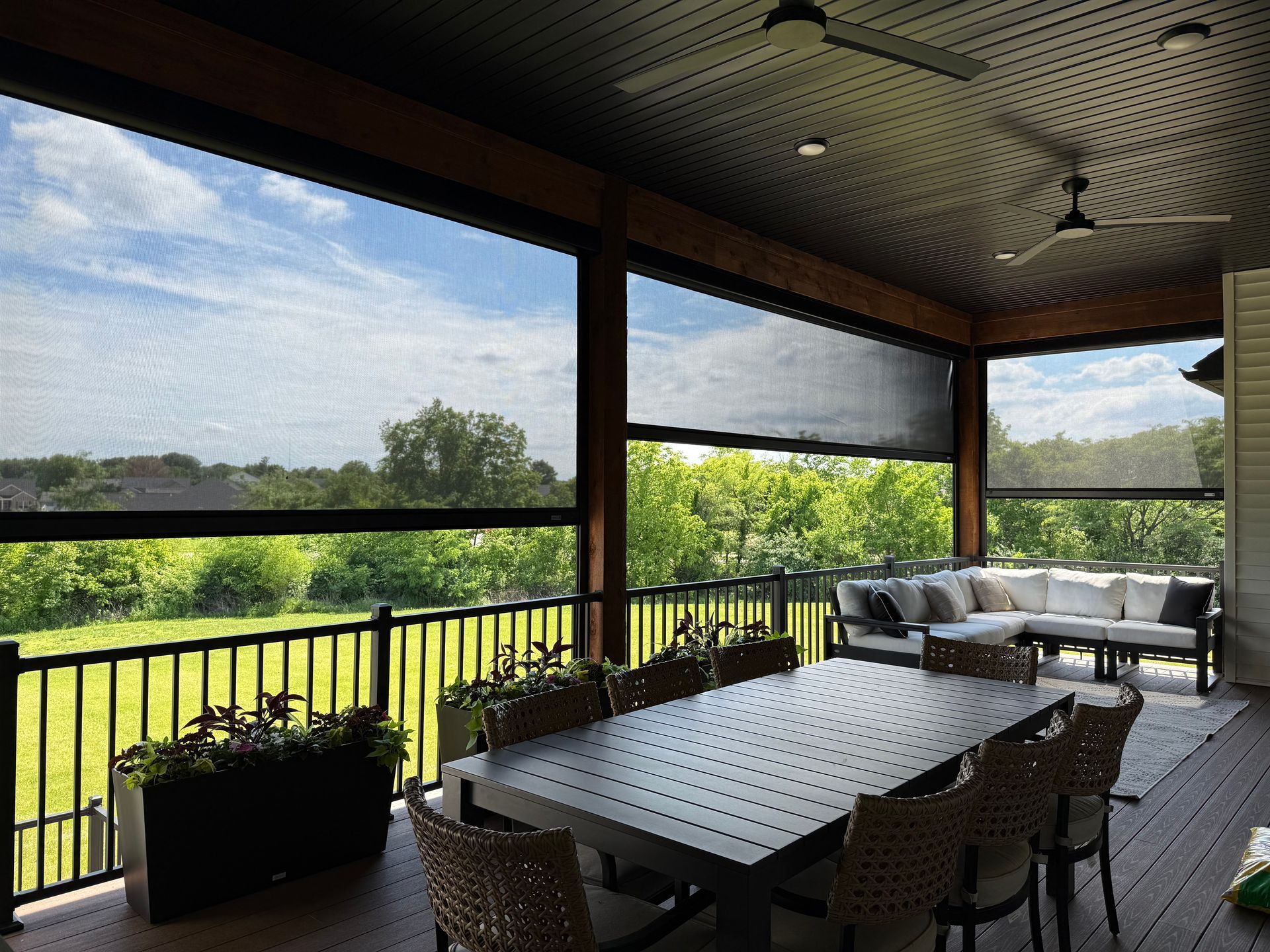 Outdoor patio with retractable screens, dining table, and sectional seating, overlooking a green landscape.