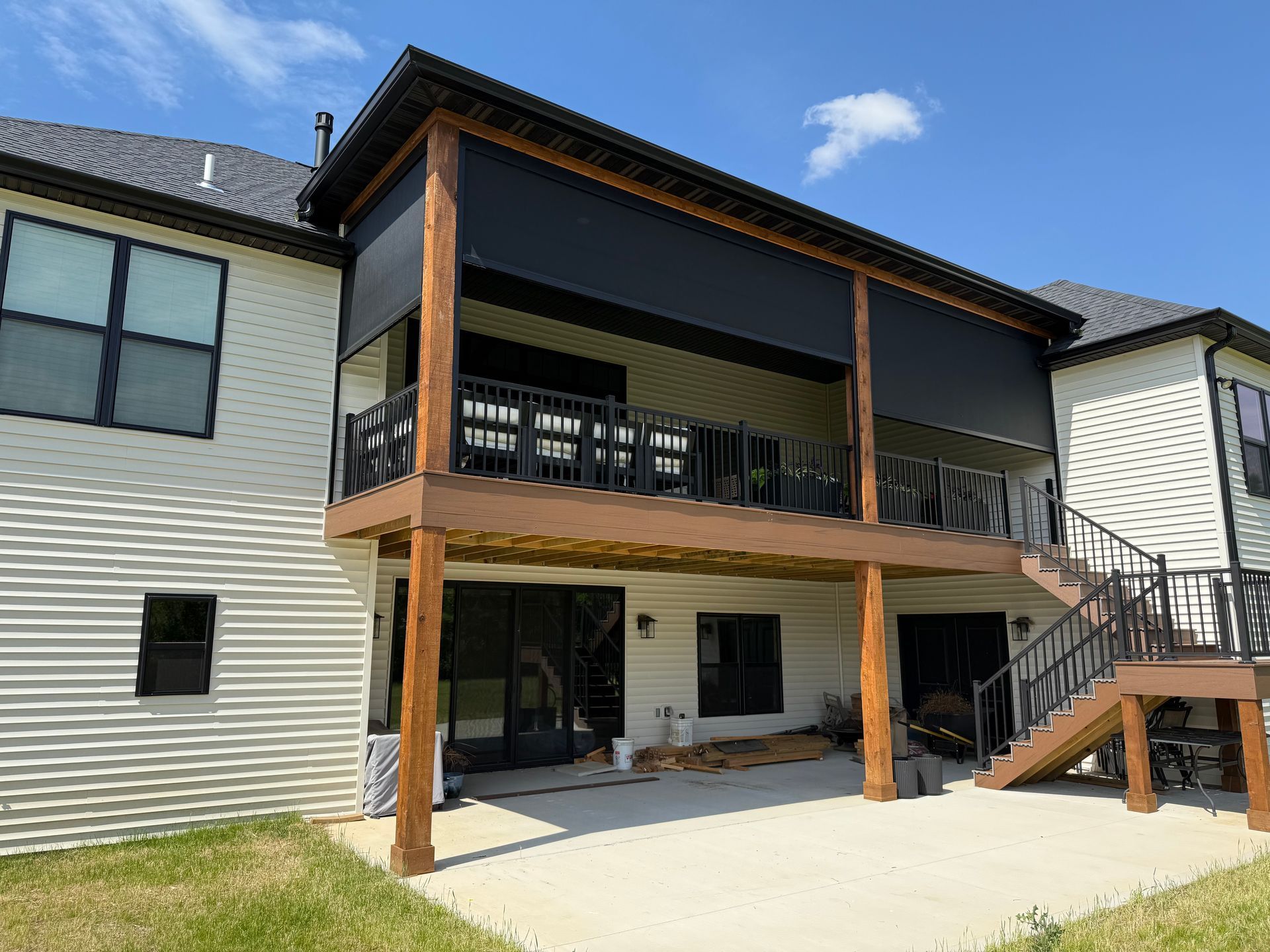 Two-story house with a wooden deck featuring black sun shades; sunny day, blue sky.