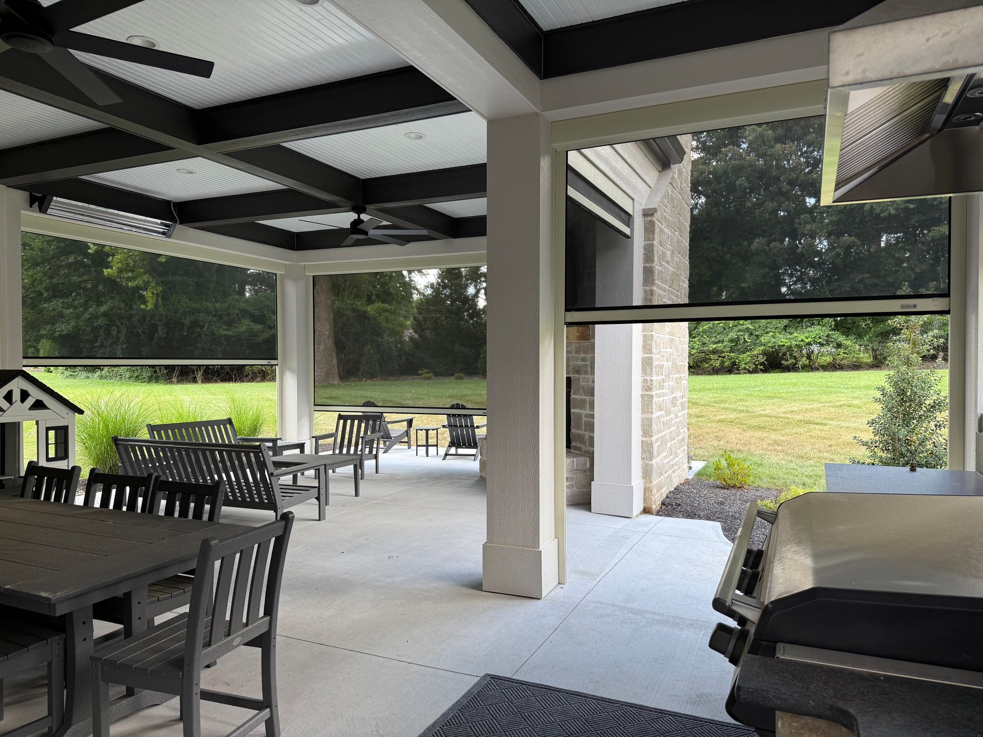 Covered patio with outdoor furniture, greenery beyond, and retractable screens.