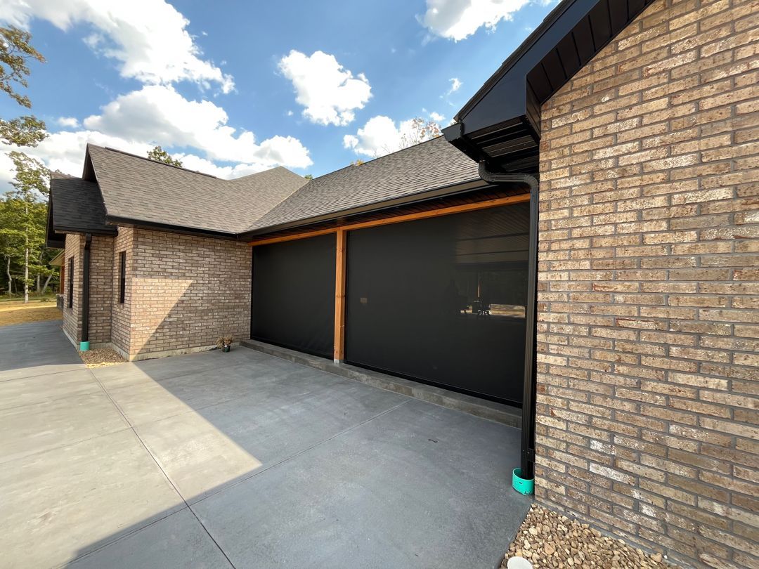 Garage with black doors, brown brick exterior, and concrete driveway under a blue sky.