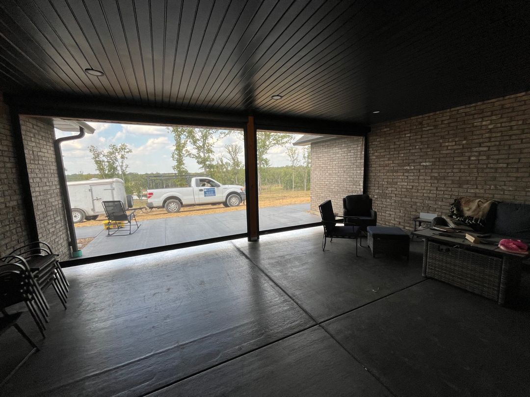 An open-air living space with rolling screens and outdoor view of a truck and trailer.