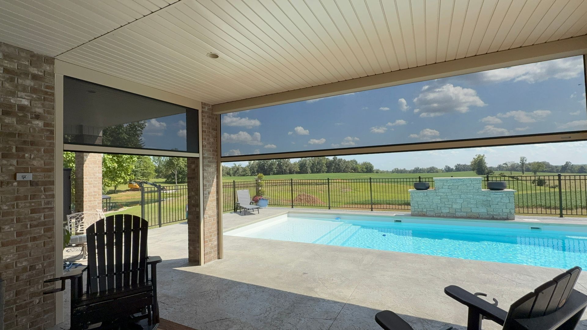 Patio with retractable screen overlooking a pool and a green field on a sunny day.