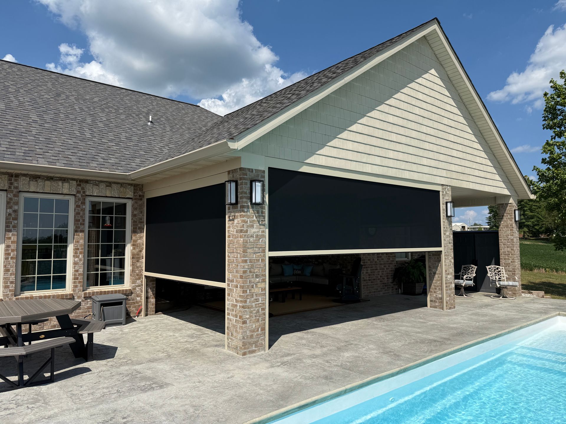 Black outdoor shades partially cover a patio overlooking a pool.