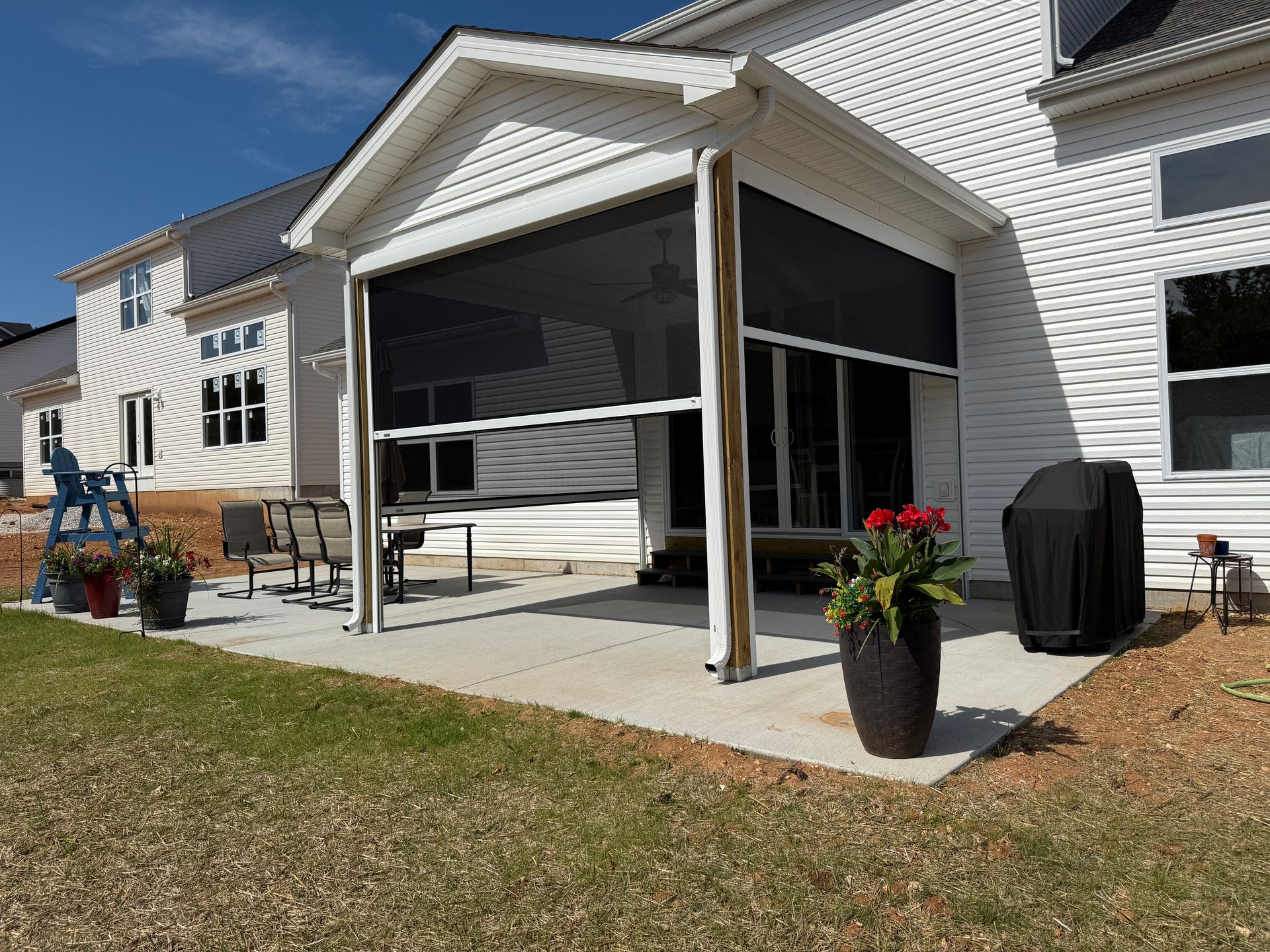 Backyard patio with retractable screen, potted plants, grill, and house.