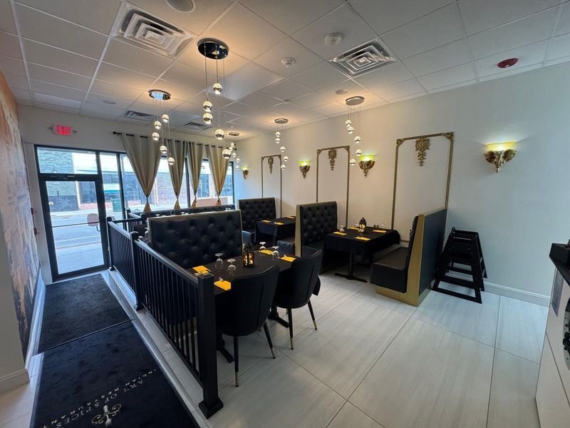 Interior of a restaurant with black booths, tables, gold accents, and white floors.