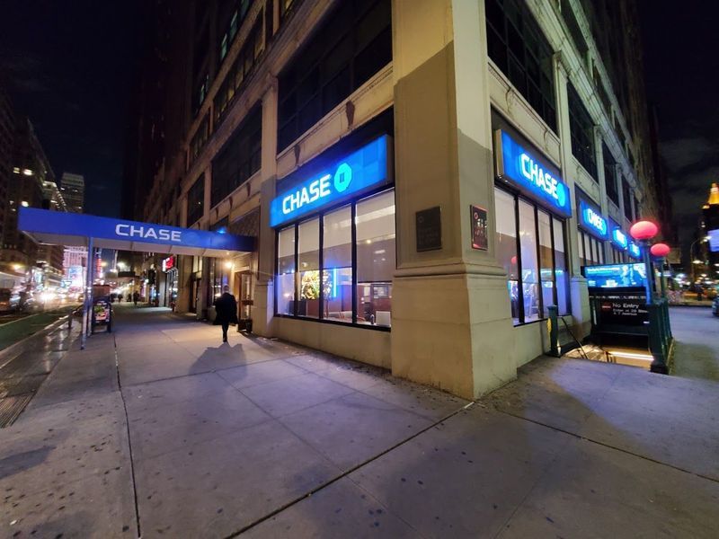 Exterior of a Chase Bank at night with illuminated blue signs; a person walks on the sidewalk.