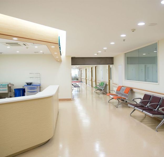 Hospital reception area with cream-colored desk, long hallway, and chairs for waiting patients.