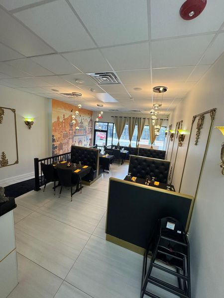 Interior of a restaurant with booths, tables, and decorative wall sconces. White walls, beige curtains, and gray tile floors.