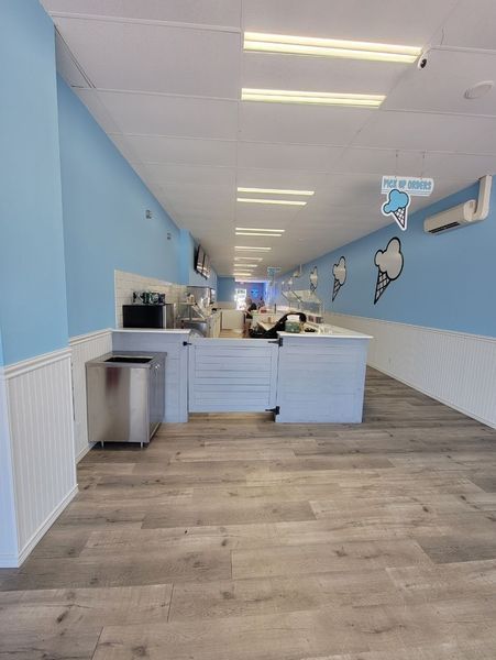 Empty ice cream shop interior with blue and white walls, and light wood flooring.