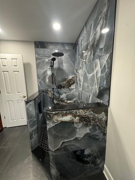 Luxurious bathroom shower with dark, marbled walls and countertops; black shower fixtures.