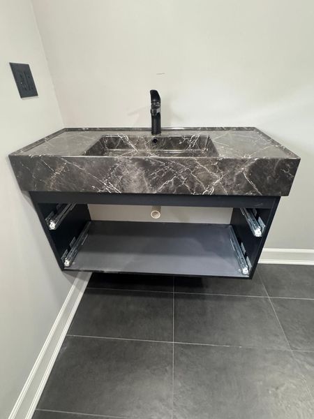 Modern, wall-mounted bathroom vanity with marble countertop, black faucet, and open storage shelf.