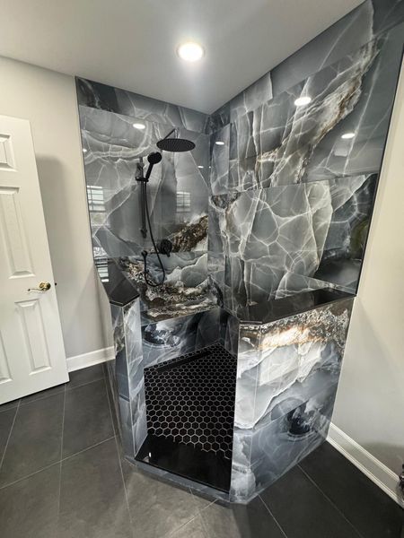 Luxurious shower with black and gray marbled tile, black shower head, and dark gray flooring.