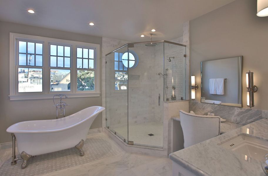 Spacious, elegant bathroom with a clawfoot tub, glass shower, and vanity with large windows, white and gray tones.