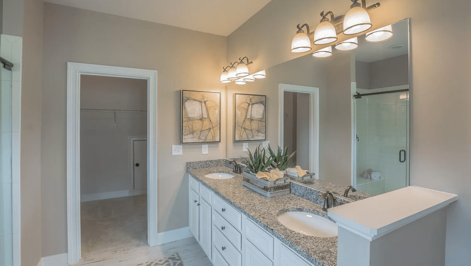 Bathroom with double vanity, gray granite countertop, white cabinets, and artwork.