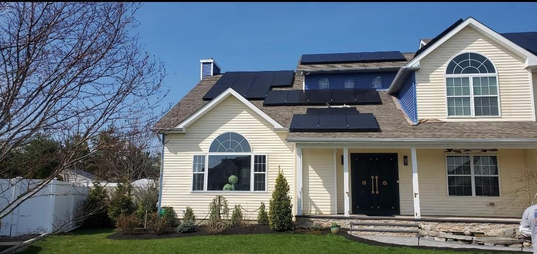 House with solar panels on the roof, green grass, clear blue sky.