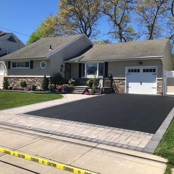 Ranch-style house with new asphalt driveway and brick border. Landscaping and garage. Blue sky.
