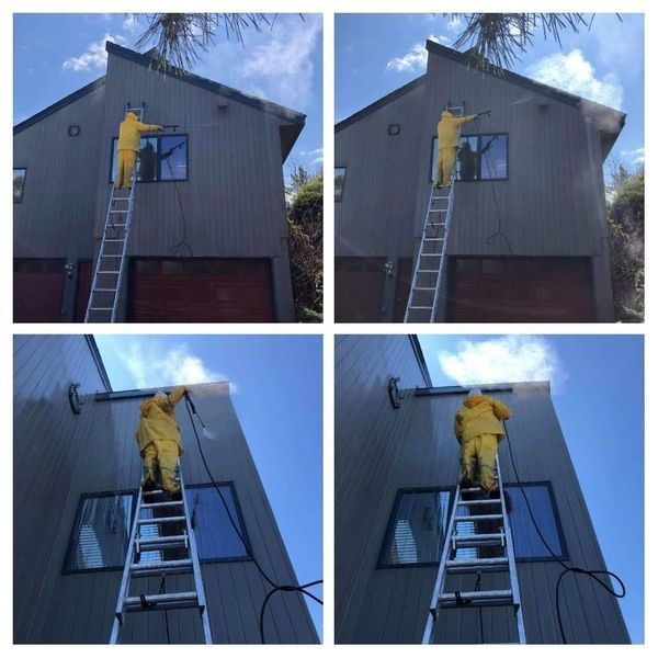 Person in yellow suit pressure washing a gray building from a ladder.