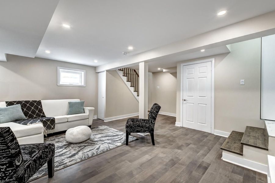 A finished basement living room with white walls, grey flooring, a white couch, and a patterned rug.