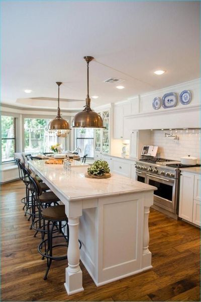 A modern kitchen with a large island, pendant lights, and bar stools. White cabinets, marble countertop, hardwood floors.