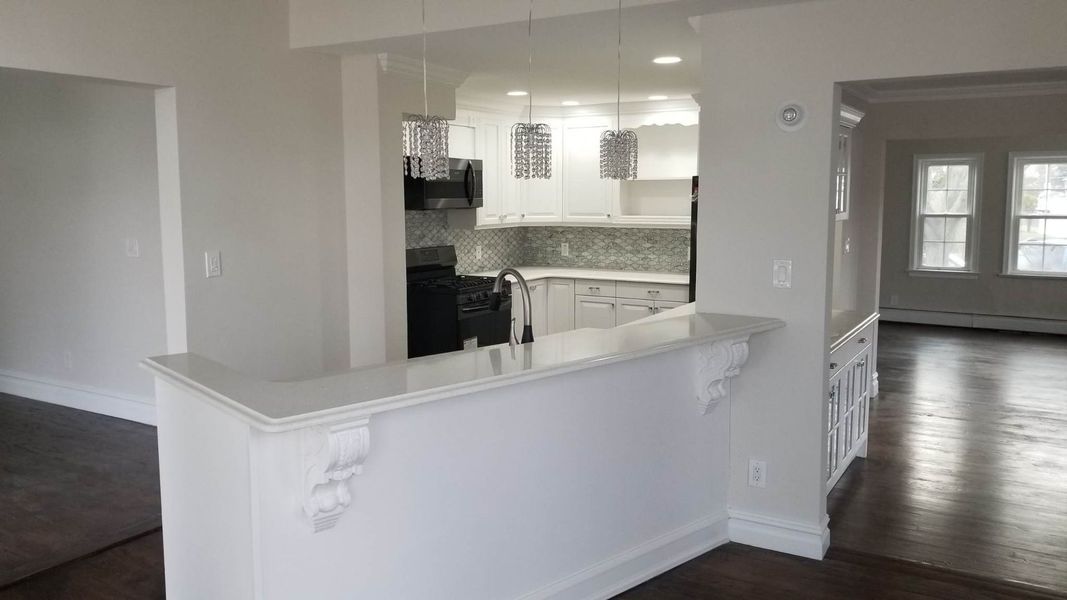 White-walled interior with kitchen view, dark floors, and a breakfast bar.
