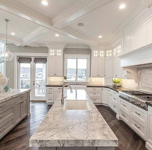 Elegant white kitchen with gray island, stainless steel appliances, dark wood floor.