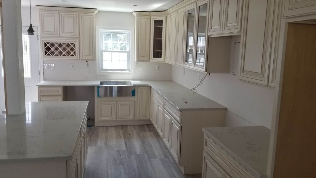 Cream-colored kitchen under construction with light countertops, cabinetry, and a window.