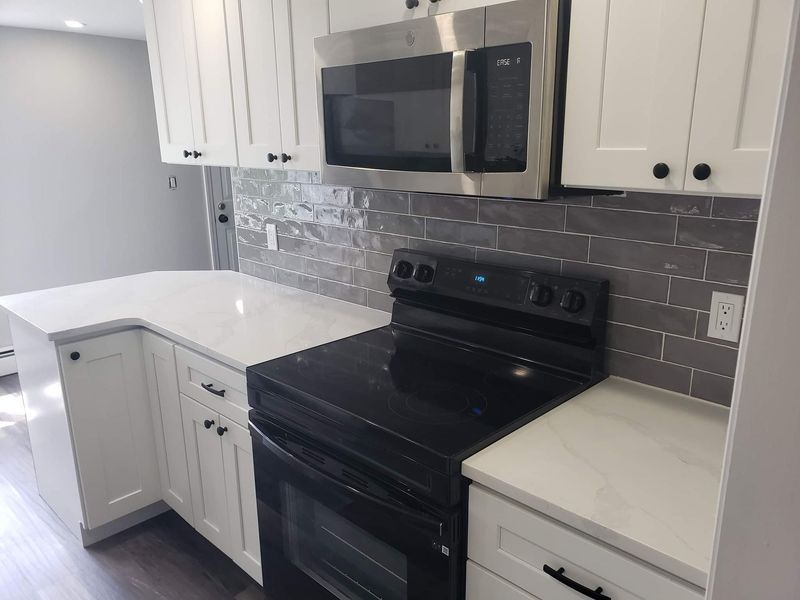 White kitchen with quartz countertops, black oven, and stainless steel microwave.