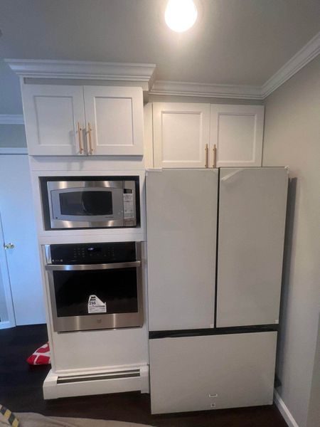 White kitchen cabinets with microwave and oven next to white refrigerator.