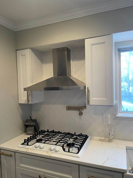 Kitchen with white cabinets, stove, and stainless steel range hood.
