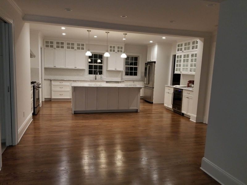 Spacious kitchen with white cabinets, island, and appliances. Dark wood floors reflect the light.
