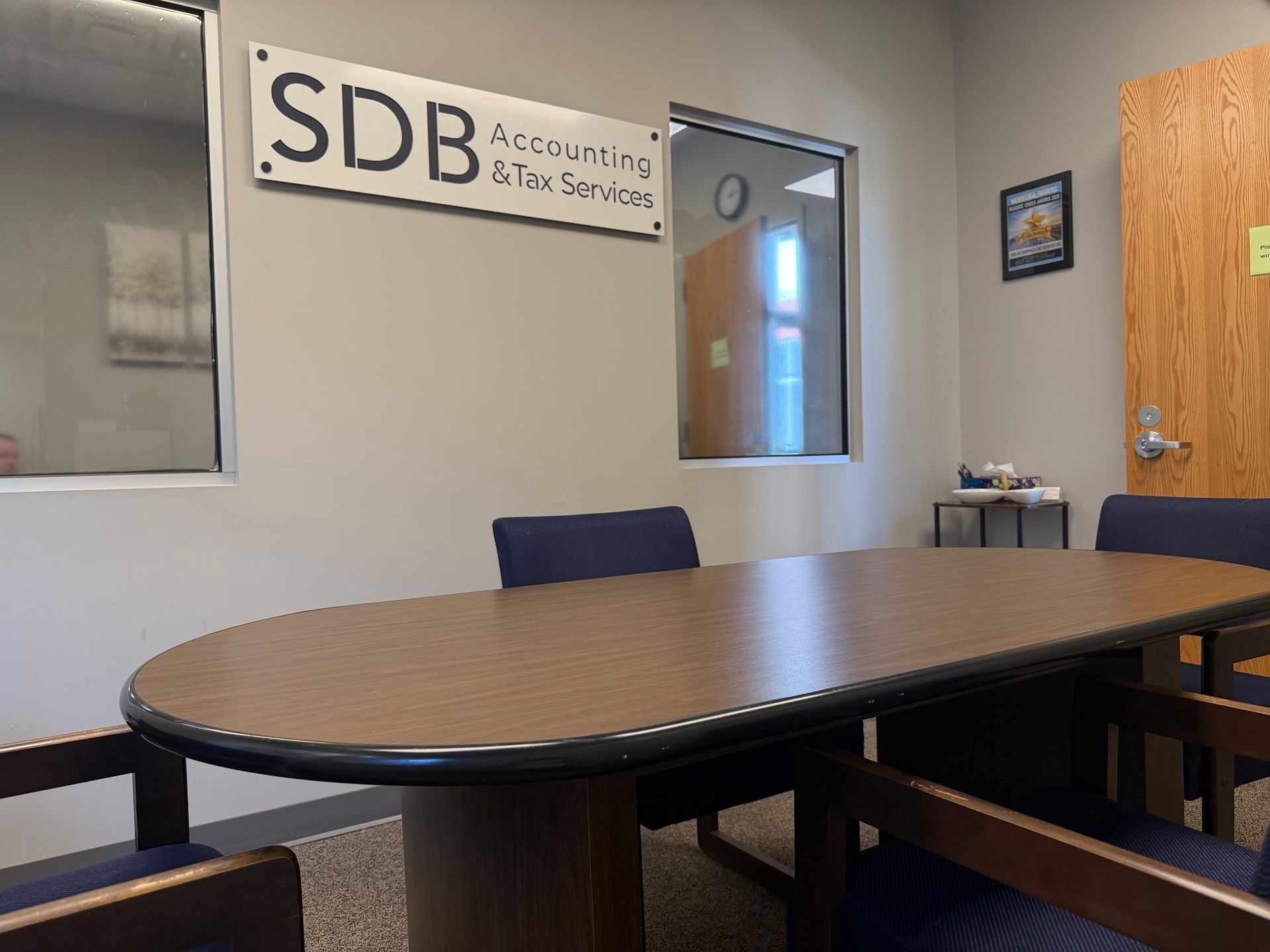 Empty conference room with oval table, blue chairs, whiteboard, and “SDB” sign on the wall.